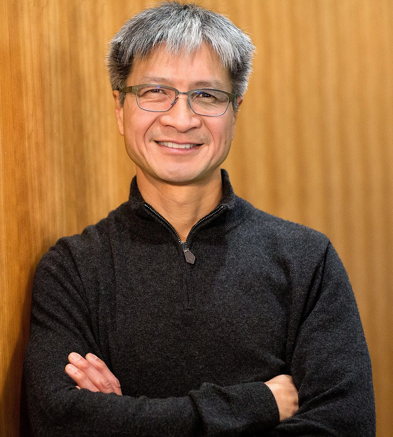 Portrait photo of Victor Peng smiling with arms crossed against a wood-paneled background